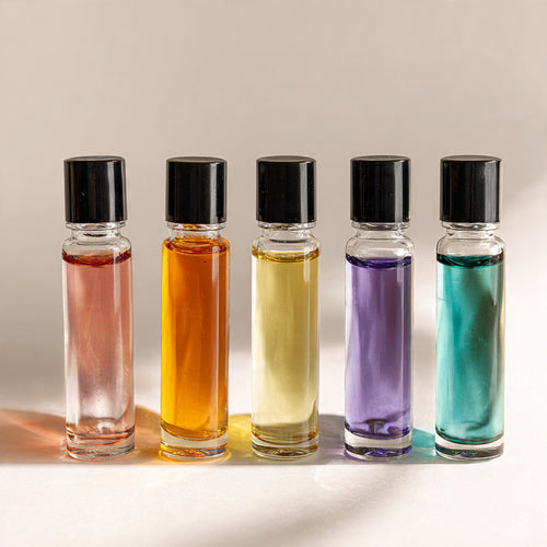 Five small glass bottles with black caps containing different colored liquids on a neutral background